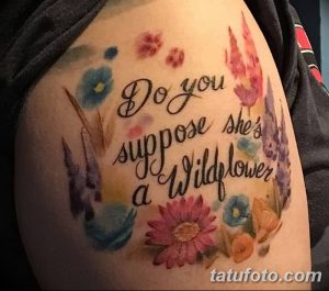 Фото тату: акварельная татуировка на плече с надписью 'Do you suppose she's a Wildflower' и изображением полевых цветов в нежных розовых и голубых тонах.