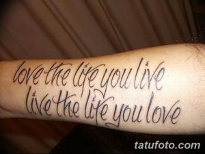 Фото татуировки на предплечье с фразой "love the life you live, live the life you love", выполненной черным шрифтом.