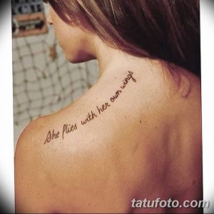 Фото татуировки с фразой "She flies with her own wings" на спине, выполненной коричневым шрифтом.