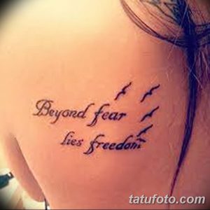 Фото тату надписи 'Beyond fear lies freedom' на боку девушки. Изящный шрифт, минималистичный дизайн, вдохновляющий смысл.