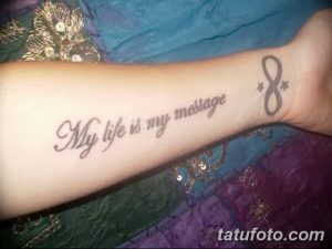 Фото тату: серая надпись 'My life is my message' на предплечье, рядом с символом бесконечности и звездами. Женская татуировка, шрифт с завитушками.