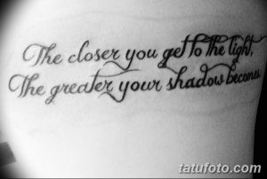 Фото тату надписи 'The closer you get to the light, The greater your shadow becomes' на боку. Черный цвет, каллиграфия, философский смысл.