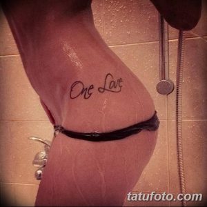 Фото тату с надписью 'One Love', выполненной изящным шрифтом на боку женщины. Небольшая, черно-белая татуировка, символизирующая единство и любовь.