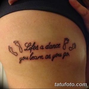 Фото тату на боку с изображением детских следов и надписью 'Life is a dance you learn as you go'. Черный цвет, минималистичный стиль, вдохновляющая фраза.