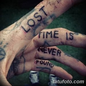 Черно-белое фото татуировки на тыльной стороне рук с фразой 'Lost time is never found'. Руки с татуировками скрещены.