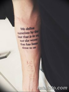 Черно-белое фото татуировки на предплечье с цитатой 'We define ourselves by the best that is in us...'.