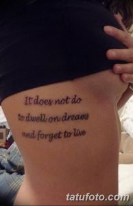 Фото тату надписи на боку: «It does not do to dwell on dreams and forget to live». Минималистичная татуировка, выполненная тонким шрифтом.