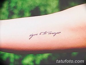 Фото тату надписи на руке: «Sigue a tu corazon». Минималистичная татуировка, выполненная тонким красным цветом.