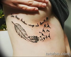 Фото татуировки с изображением пера, вылетающих птиц и цитаты 'Take these broken wings and learn to fly' на боку девушки.