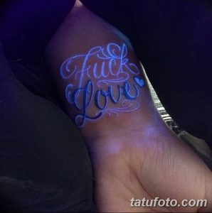 Фото тату: светящаяся в ультрафиолете надпись 'Fuck Love' на запястье. Смелый и провокационный рисунок с голубыми оттенками.