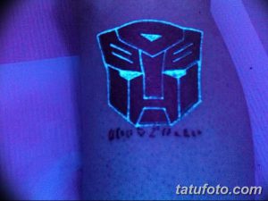 Фото тату: логотип автобота из вселенной Трансформеров, выполненный в технике UV татуировки на спине. Неоновое свечение под ультрафиолетовым светом.