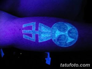 Фото тату: минималистичная UV татуировка на руке, изображающая стрелу, направленную в сферу. Неоновое свечение под ультрафиолетовым светом.
