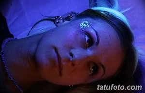 Фото тату кельтского узла, выполненного светящейся краской под ультрафиолетом на лице. Эскиз татуировки с переплетающимися линиями и сложным узором.