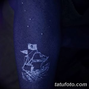 Фотография татуировки в виде старинного парусника на руке, выполненной светящимися в ультрафиолете красками. Рисунок украшен звездами и напоминает морской пейзаж.