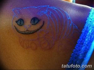 Фотография татуировки Чеширского Кота, выполненной светящимися в ультрафиолете красками на спине. Рисунок детализирован и имеет яркий, загадочный вид.