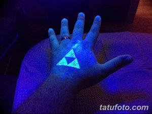 Фото ультрафиолетовой татуировки с изображением символа Трифорс из игры The Legend of Zelda, светящегося в темноте под воздействием ультрафиолетового света. Татуировка выполнена на ладони.