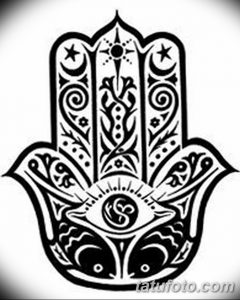 Черно-белое фото тату, изображающее Хамасу с открытым глазом в центре, украшенную сложным орнаментом и символами.