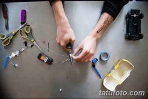 Фотография процесса сборки самодельной тату-машинки. Видны руки мастера, держащего плоскогубцы и работающего с проводами.