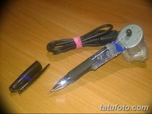 Фотография самодельной тату-машинки, сделанной из ручки и обмотанной изолентой. Рядом лежит стержень от ручки.
