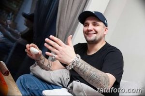Фотография Басты, аплодирующего руками, покрытыми татуировками с надписями и узорами.