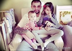 Фотография мужчины с татуировками, сидящего в кресле с маленькой дочкой и сыном. Теплая семейная сцена, демонстрирующая любовь и заботу.