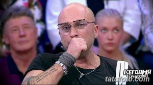 Фото тату на руке мужчины в очках. Видна надпись на латыни и небольшие символы, выполненные в черном цвете. Стильный и выразительный рисунок.