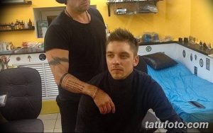 Фотография процесса нанесения татуировки. Виден мастер тату и клиент, татуировка на руке в процессе работы, тату-салон.