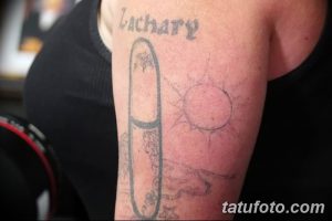 Фото татуировки на руке: изображение скейтборда, солнца и надписи 'Zachary', выполненные в нечетком и размытом стиле. Татуировка выглядит незаконченной.