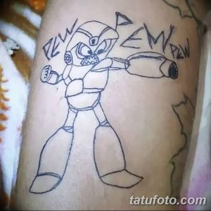 Фото татуировки на руке: изображение персонажа Mega Man из видеоигры, выполненное в черно-белом графическом стиле. Вокруг персонажа надписи 'PEW PEW'.