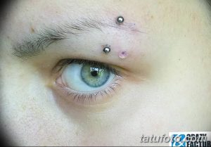 Фото пирсинга брови с двумя серебристыми украшениями. Крупный план глаза и брови, демонстрирующий аккуратность и эстетику пирсинга.