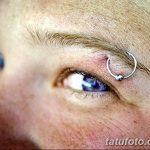 Фото тату: пирсинг брови с использованием серебряного кольца. Акцент на глазе и брови, минималистичный стиль.