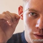 Фото процесса подготовки к пирсингу брови у молодого человека. Видно, как мастер отмечает точку прокола с помощью маркера.