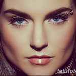Фотография крупным планом лица девушки с пирсингом брови и губы. Пирсинг выполнен серебристыми кольцами и штангой, подчеркивающими выразительность глаз и чувственные губы.
