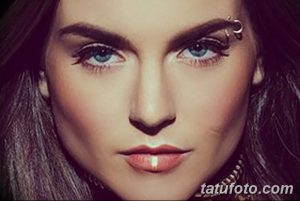 Фотография крупным планом лица девушки с пирсингом брови и губы. Пирсинг выполнен серебристыми кольцами и штангой, подчеркивающими выразительность глаз и чувственные губы.