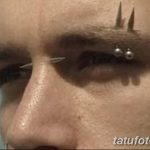 Фото тату: сложный пирсинг на лице мужчины, включающий проколы над бровью, на лбу и в области глаза. Экстремальный стиль.