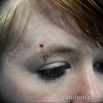 Фото пирсинга брови с двумя серебристыми украшениями. Крупный план женского лица с акцентом на глаза и пирсинг.