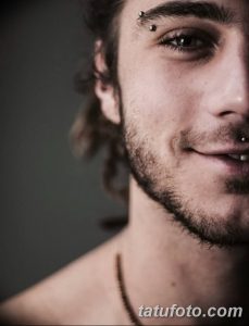 Фотография пирсинга брови и губы с использованием серебряных украшений. Крупный план лица молодого человека с бородой.