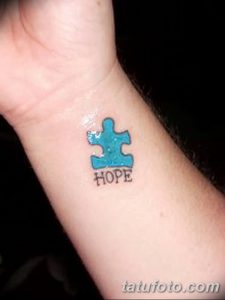 Фото тату: голубой элемент пазла на запястье с надписью 'HOPE'. Минималистичный рисунок татуировки, выполненный опытным мастером.