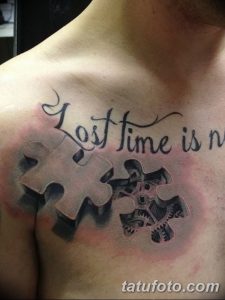 Фото тату: Черно-серая татуировка в виде пазла с надписью "Lost time is never found again" на груди мужчины.