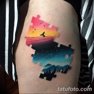 Фото тату на руке с изображением элемента пазла, внутри которого находится пейзаж с горами, лесом и небом. Красочные цвета и реалистичная проработка.