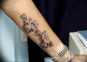 Фото татуировки на запястье: два элемента пазла с буквами 'R' и 'K', выполненные в черно-серых тонах.