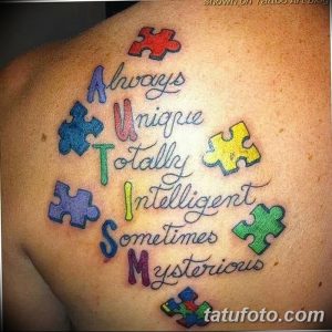 Фото цветной татуировки пазла с надписью 'Always Unique Totally Intelligent Sometimes Mysterious' на плече. Символ поддержки людей с аутизмом.