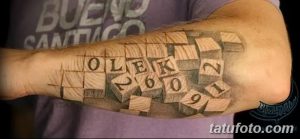 Фото тату даты рождения "OLEK 26.09.91" в виде кубиков на предплечье. Черно-белый рисунок татуировки с реалистичной детализацией.
