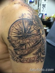 Фото тату компаса на плече с надписью 'Not all those who wander are lost'. Черно-серый рисунок с розами и лентой.