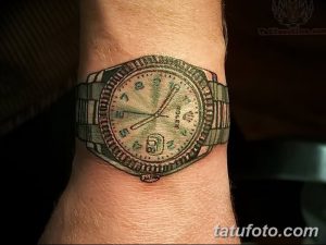 Небольшая татуировка на запястье с изображением часов Rolex. Реалистичный рисунок татуировки, выполненный в серых и зеленых тонах.