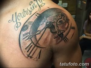 Фото тату на плече: часы с открытым механизмом и надписью 'Yours in time', выполненные в черно-серых тонах. Реалистичный рисунок татуировки.