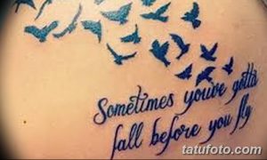 Фото тату стаи голубых птиц и надписи 'Sometimes you've gotta fall before you fly' на спине. Минималистичный дизайн, выполненный в голубых тонах.