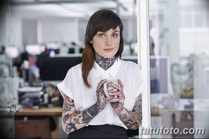 Фото девушки с множеством татуировок на руках и шее, работающей в офисе. Современный и стильный образ.