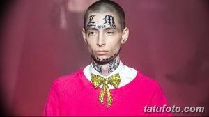 Фото татуировки на лице и шее, включающей надписи и узоры в готическом стиле, выполненной черными чернилами на бледной коже.