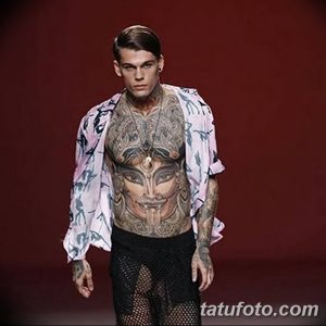 Фото тату: мужчина с масштабной татуировкой, покрывающей лицо, шею, грудь и руки. Реалистичное изображение лица, сложные узоры.